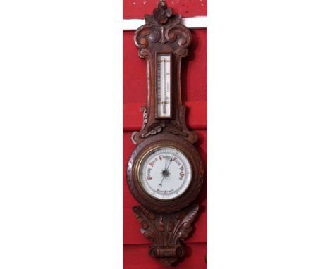 Late 19th century carved oak aneroid wheel barometer, of floral and foliate detail set with a single scale porcelain backed m