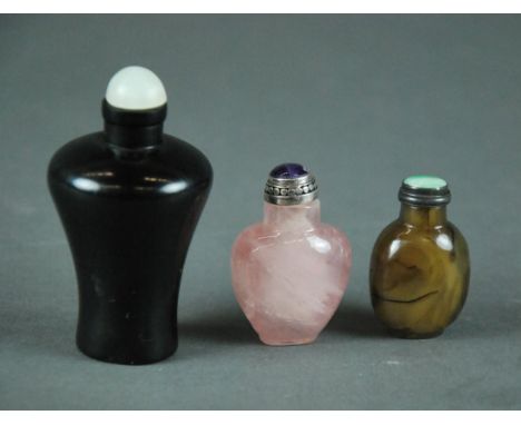THREE CHINESE CARVED SNUFF BOTTLES Comprising a small well hollowed rose quartz example of ovoid form with short rounded shou