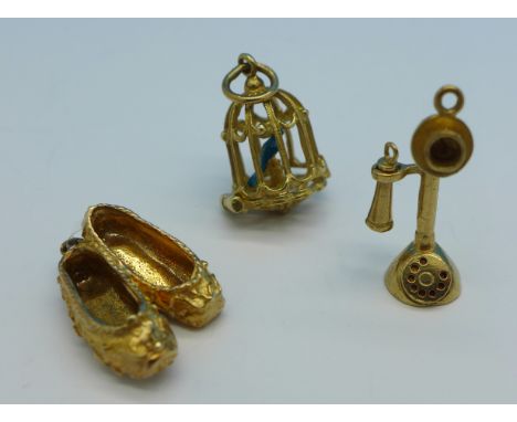 Three hallmarked 9ct gold charms, a candlestick telephone, ballet shoes and a birdcage with bird, 9.6g