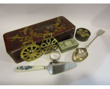 A Japanese lacquered trinket box containing assorted items including a silver napkin ring plated serving spoon, horse brasses