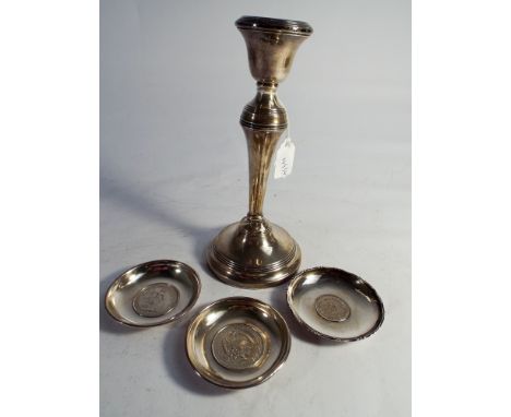A hallmarked silver candlestick with fixed sconce and 3 white metal ashtrays inset with Mexican silver dollar and one other i