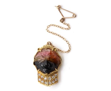A carved watermelon tourmaline and diamond brooch,with a carved lion head vari coloured tourmaline, claw set to an incised bo