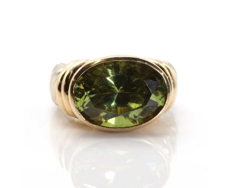 A gold olive green cubic zirconia ring, an oval mixed cut cubic zirconia, 10.89mm x 14.80mm, bezel set to banded shoulders an