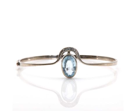A white gold sky blue topaz and diamond hinged bangle,centring an oval mixed cut sky blue topaz bezel set to a plain collet, 