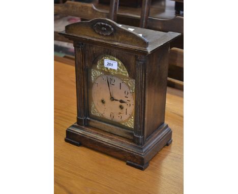 An early 20th century oak mantel clock, silvered dial, Arabic numerals, arched pediment, stepped base