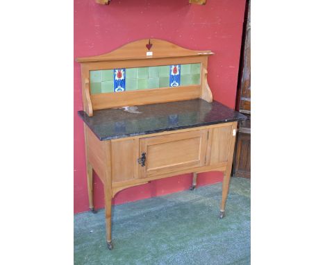 An Art Nouveau satinwood tile back wash stand, variegated black marble top, single panel door, tapering supports, ceramic cas