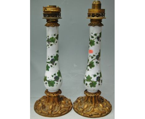 A pair of Victorian pedestal lamp bases, each having a glass stem painted with leaves and berries, on gilt metal bases