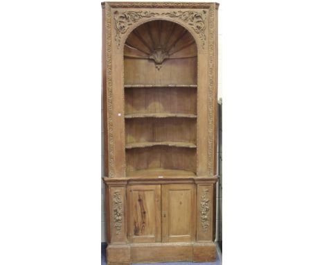 A late 19th Century pine barrel-backed corner cabinet, the arched open shelf with carved shell surmount and foliate spandrels