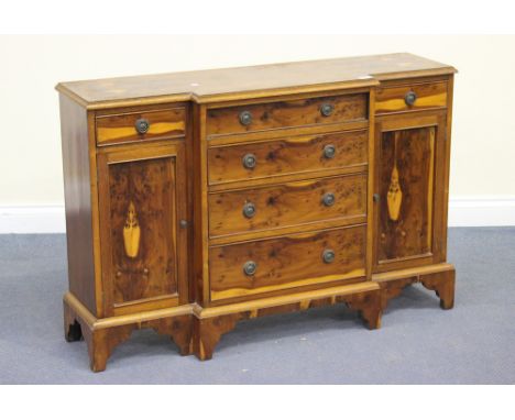 A 20th Century reproduction yew breakfront sideboard, fitted with an arrangement of drawers and cupboards, on shaped bracket 