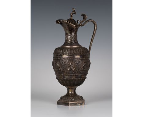 A late 19th Century Indian silver claret jug, possibly Kutch, the urn shaped body and neck cast in relief with a band of deit