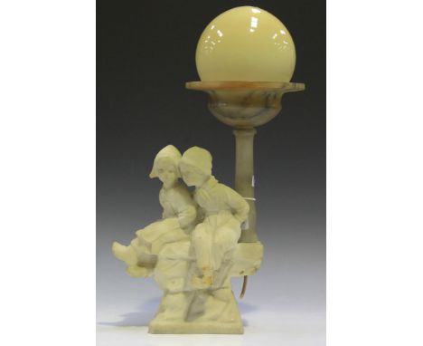 An early 20th Century carved alabaster figural table lamp in the form of a Dutch girl and boy seated upon a wall, height appr