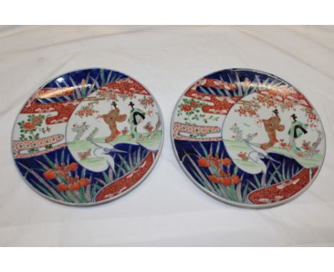 A pair of Japanese Imari pottery circular chargers with female, bird and landscape decoration, 12" diameter