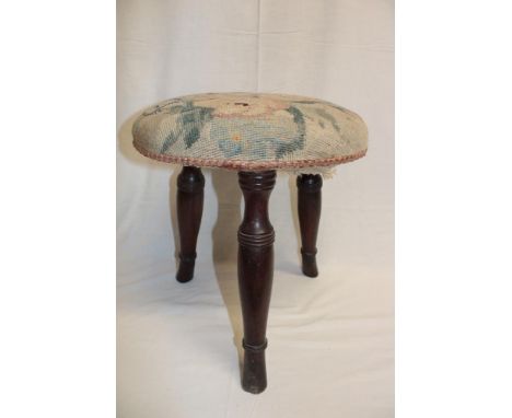 An old mahogany three-legged stool with tapestry upholstered floral seat