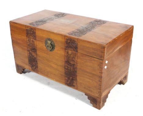 A camphor wood trunk. Having two heavily carved bands of decoration featuring oriental landscapes and a brass latch, on brack