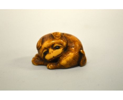 A JAPANESE IVORY NETSUKE, carved in the form of a pug curled up, the eyes inlaid, signed to base