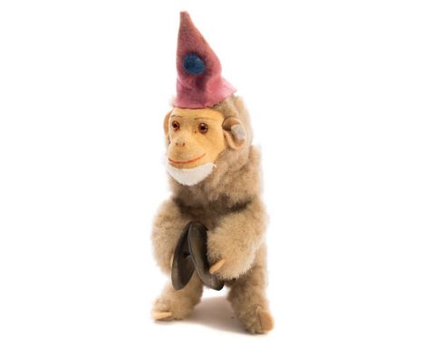 An early 20th century Schuco style clockwork monkey:, with felt hat and face , glass eyes and painted face, playing a pair of