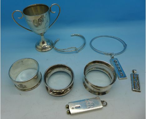 Three silver ingots, a silver trophy, two silver bangles and three silver napkin rings, 145g, one bangle set with three small