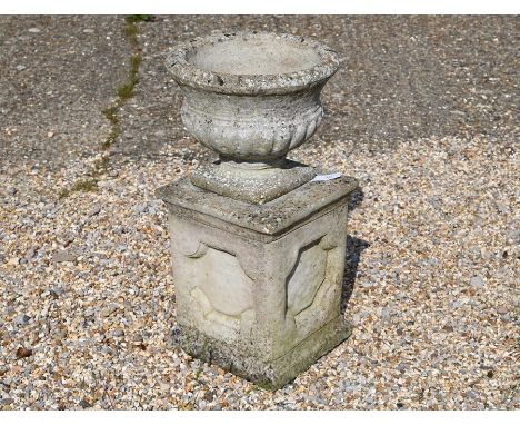 A weathered stone-cast garden urn planter on square plinth base