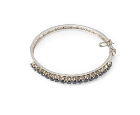 A sapphire set bangle  of hinged design, claw set with a row of eighteen round cut sapphires, with concealed clasp and safety