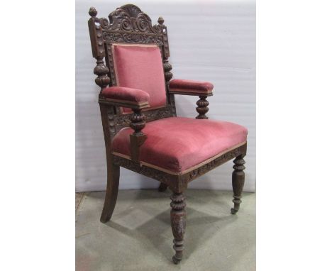 A Victorian oak armchair with carved frame, short arms, pink dralon upholstered seat, back pad and arm rests raised on turned