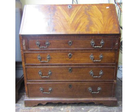 A Georgian mahogany bureau of four long graduated drawers, the fall flap with well matched flamed veneers, enclosing the orig