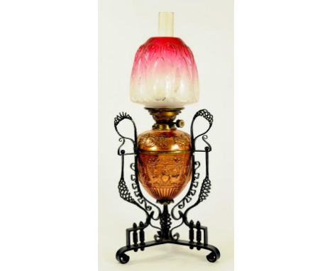 AN ARTS AND CRAFTS EMBOSSED COPPER AND WROUGHT IRON OIL LAMP, THE SHADED CRANBERRY GLASS TULIP MOULDED SHADE ETCHED WITH KATE