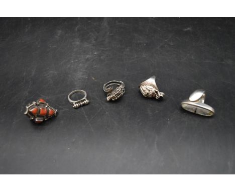 A collection of five silver rings. Including a silver dress ring inlaid with coral, a Chinese silver dragon ring and three ot