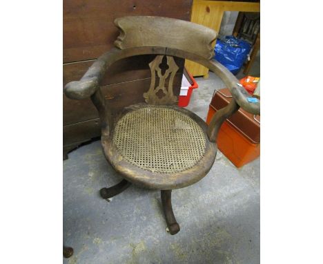 An early 20th century oak captain's chair with cane seat, on ceramic castors 