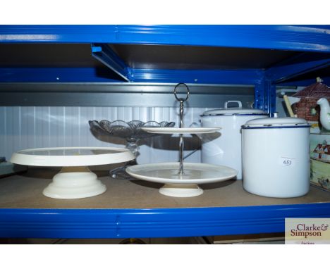 A glass cake stand together with two pottery cake stands and two enamel storage containers