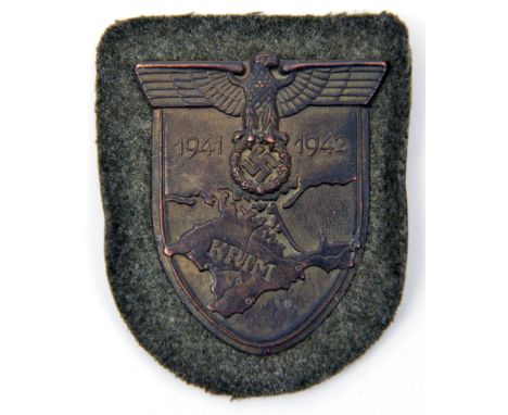 A Third Reich Krim shield, of bronzed iron on field grey cloth patch, with original paper backing marked “JFS 42” in white. U