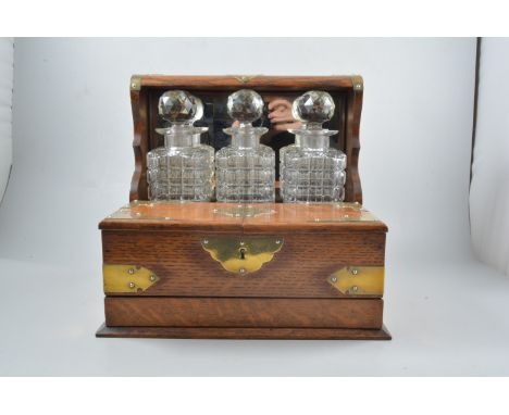 An oak three bottle tantalus with brass mounts and handles, hinged twin compartment to base with four section interior and pr