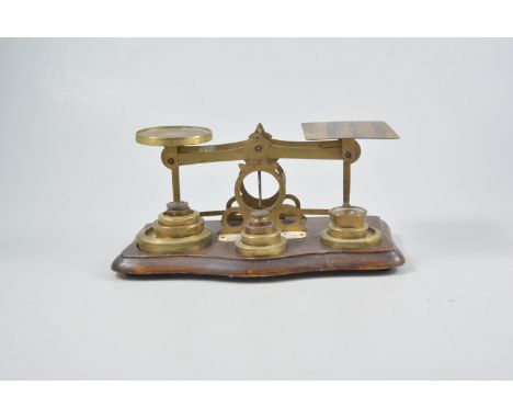 Set of brass postal balance scales, wooden base, width 25cm and weights.
