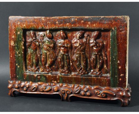 CHINESE SANCAI BRICK OR TILE, Tang style, cast with five figures under a treacle glaze with green highlights to the dresses, 