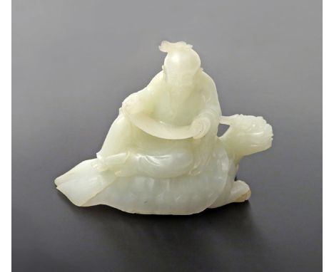 A CHINESE PALE CELADON JADE MODEL OF A SAGE 20TH CENTURY Reading a scroll while seated on the back of a horned turtle, 11.5cm