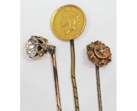 A group of three stick pins comprising one set with a United States gold dollar, one set with rose cut colourless paste and o