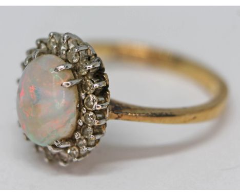 A hallmarked 9ct gold opal and diamond cluster ring featuring a central oval opal cabochon and surrounded by 20 round brillia