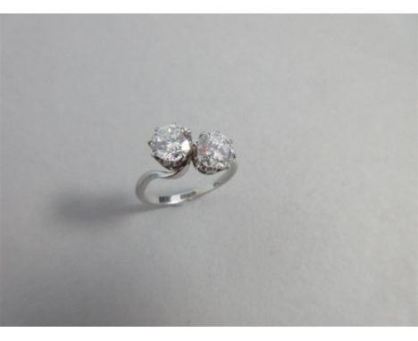 A two stone diamond ring, the two round brilliant cut diamonds claw set obliquely with the plain shank tapering to curve arou