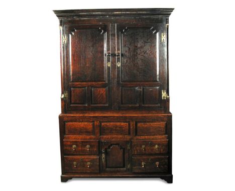 A George III oak hanging cupboard, with panelled doors above, a small central cupboard and four small drawers to the base, on