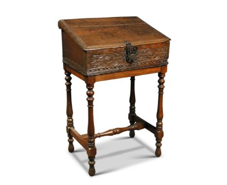 A 17th century carved oak Bible box, having sloping hinged lid above a carved front panel, on a later stand with turned and j