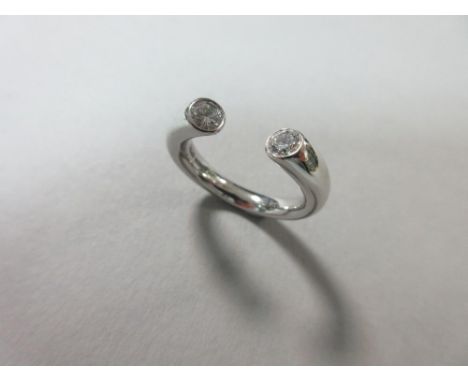 A contemporary two stone diamond ring set in platinum, designed as an incomplete hoop, the oval section band becoming round a