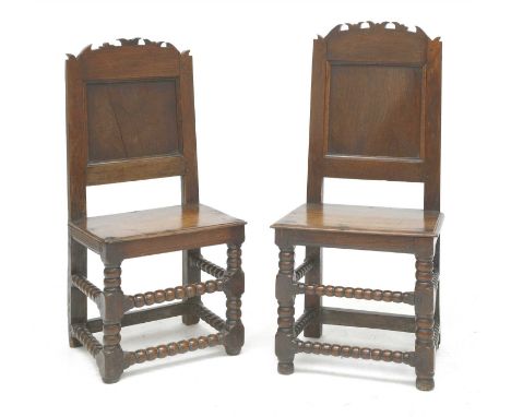 A pair of oak back stools, 17th/18th century, the panelled backs with carved, arched top rails, over solid seats and bobbin t