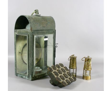 A glass and metal lamp marked 'Glasgow' along with two brass miniature miners lamps and a wooden fabric press.