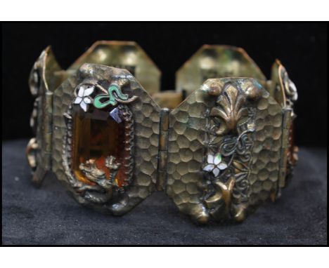 A Czech Gablonz planished 6 panel metal and enamel bracelet set with amber glass and decorated with enamel foliates and drago