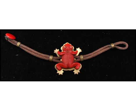 A 1940s bakelite figural bracelet strung with a red carved bakelite frog set on a brass mount with braided cord and bakelite 