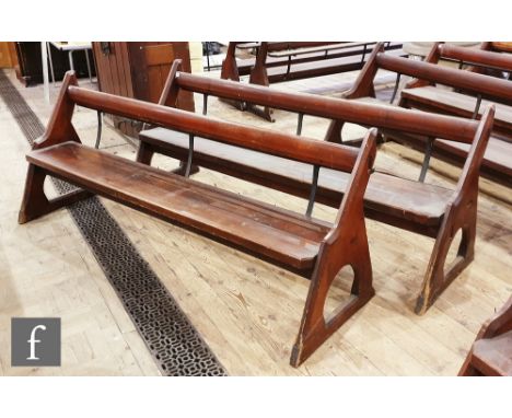 A pair of stained pine pews each with iron bar supports and book shelf on shaped open ends, height 88cm x depth 67cm x length