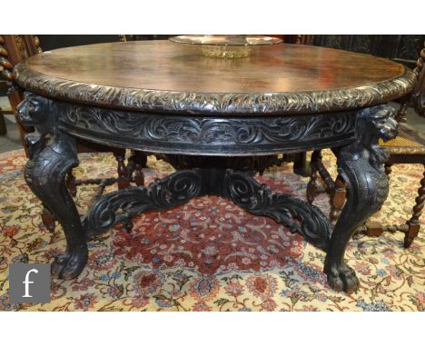 A large circular oak dining table on lion mask cabriole legs terminating in claw feet united by a stretcher centered by a fin