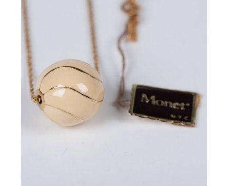 Gold-toned chain with an enameled ball-shaped pendant in ivory color, accentuated by gold-toned wavy lines. Includes Monet ha