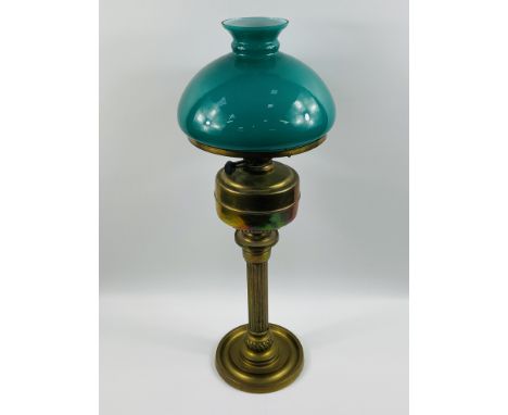 A tall brass oil lamp with a reeded column and circular base, complete with a green glass shade, 70cms high x 25cms shade dia