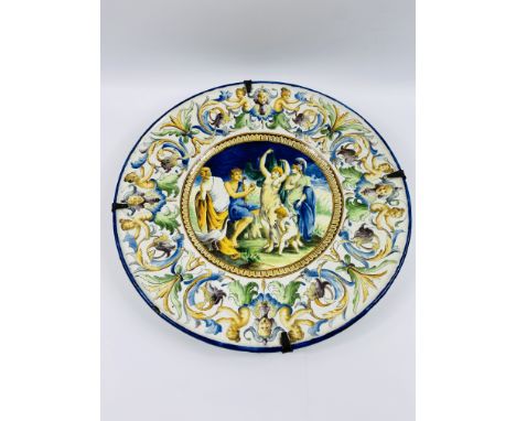 A large 19th century Italian polychrome majolica charger, with a central painted figural group, surrounded by a mask and scro