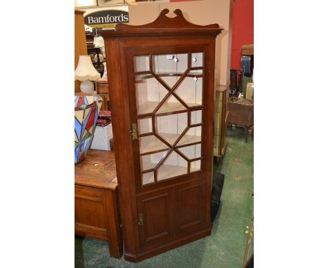 An early 20th century mahogany floor standing corner cabinet, swan neck pediment, canted angles, astragal glazed door to top,